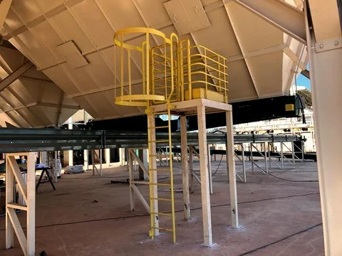 Plataforma e escada metálica com guarda-corpo amarelo em galpão